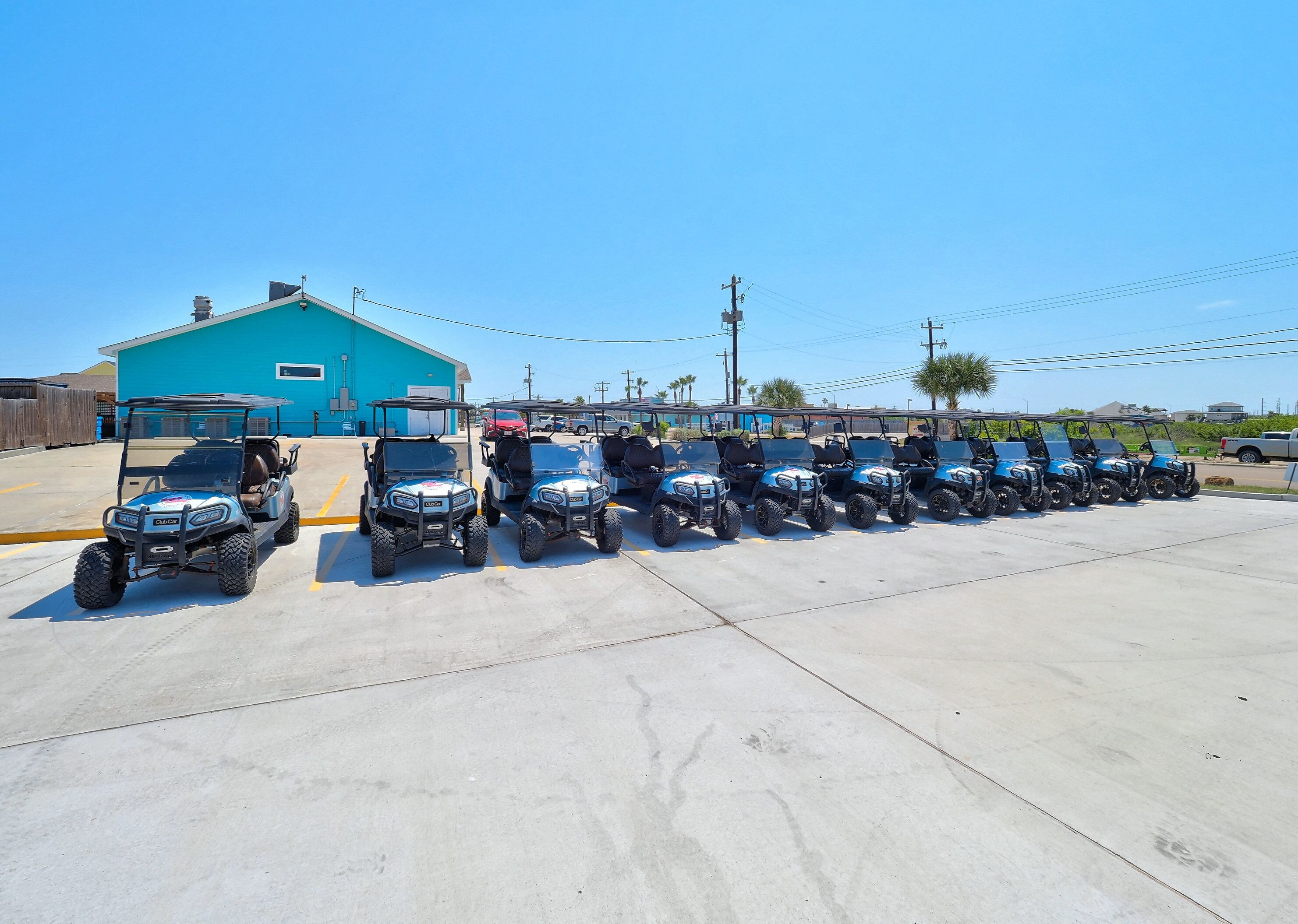 A row of golf carts parked in a lot with a blue building in the background.