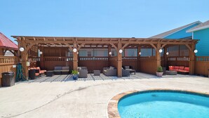 A covered outdoor area with a pool, wooden pergola, and various seating arrangements. - Ocean's Edge Hotel, Port Aransas,TX (Port Aransas)