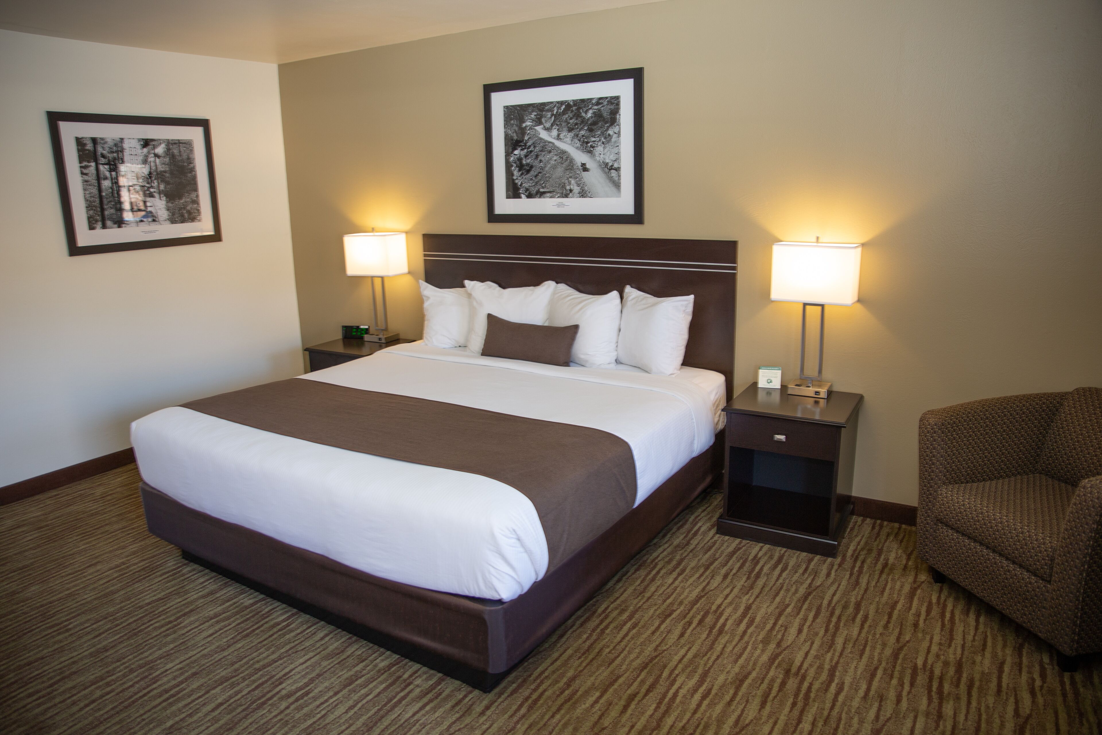 A hotel room with a large bed, two bedside tables with lamps, a chair, and two framed pictures on the walls.