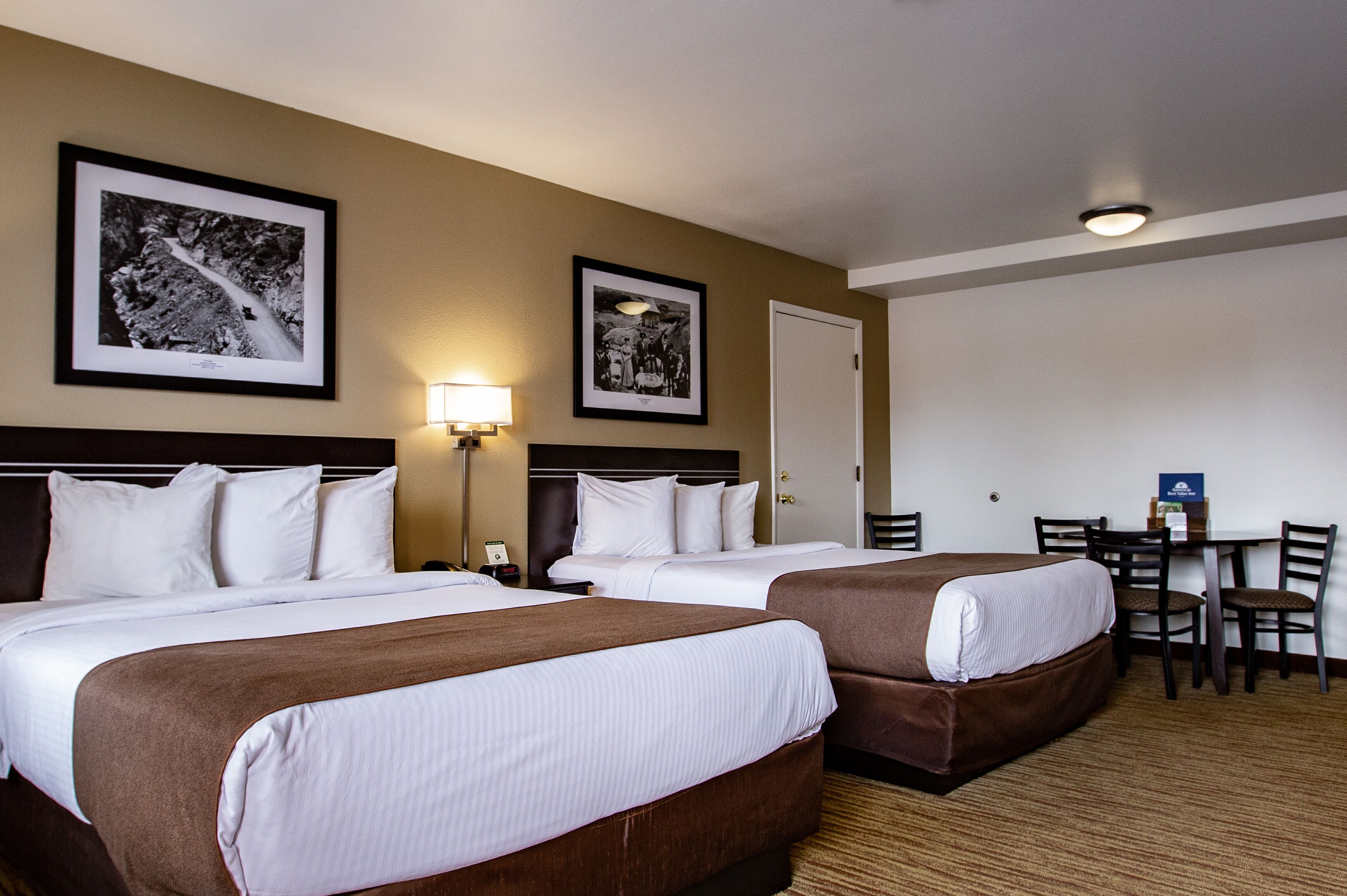 Habitación de hotel con dos camas, un escritorio y sillas. En la pared hay cuadros enmarcados.