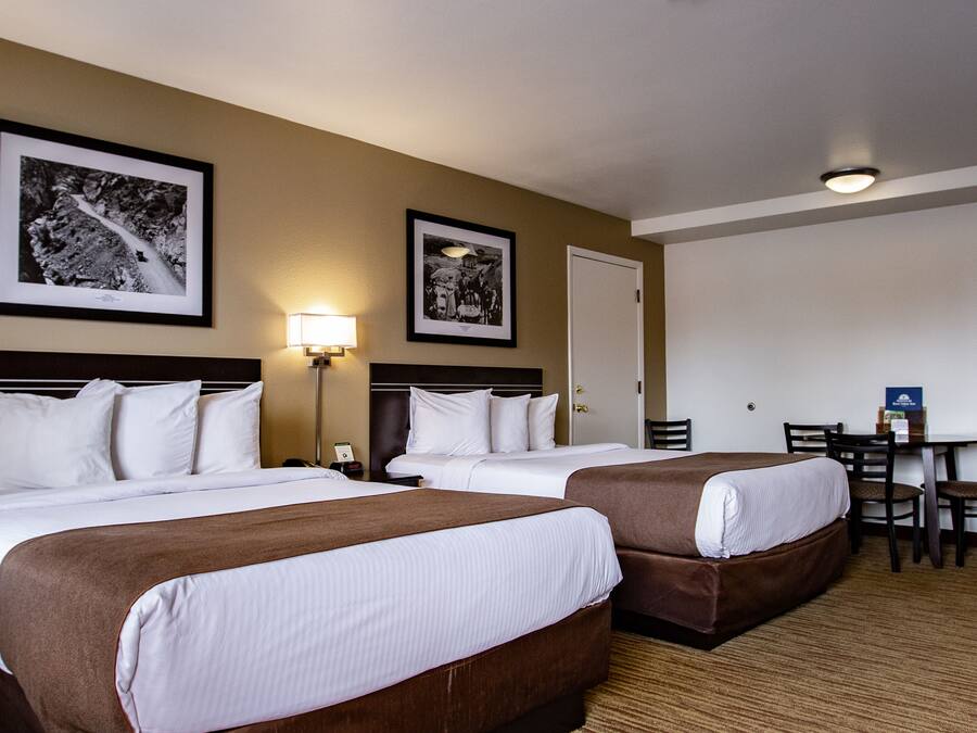 Habitación de hotel con dos camas, un escritorio y sillas. En la pared hay cuadros enmarcados.
