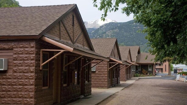 A row of log cabins with pitched roofs and wooden beams, set against a backdrop of mountains. - Villa Motel at Manitou Springs (Manitou Springs)