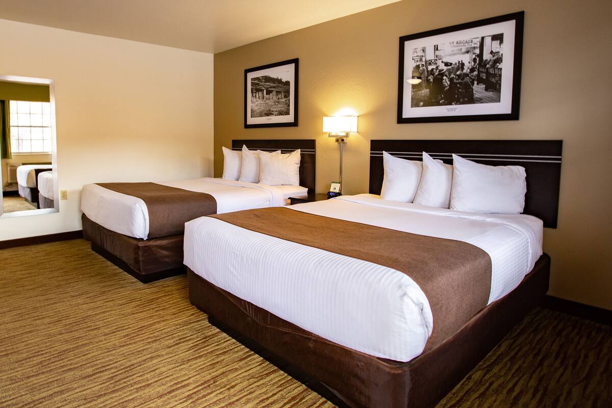 A hotel room with two beds, a nightstand with a lamp, and framed pictures on the wall.