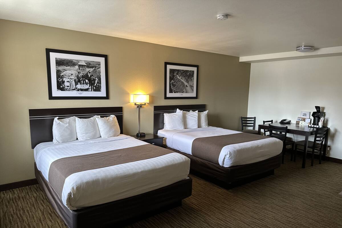 A hotel room with two beds, a desk, and a chair. There are framed pictures on the wall.