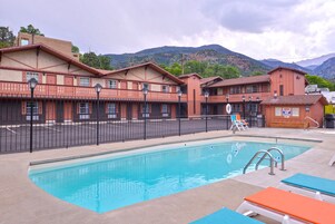 Un hotel con piscina, mobiliario exterior y montañas al fondo.