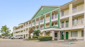 A multi-story motel with a green roof, multiple balconies, and a parking area with several vehicles. - Siegel Select Baton Rouge (Baton Rouge)