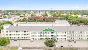 A multi-story motel with a green entrance, parking lot, and surrounding greenery. - Siegel Select Baton Rouge (Baton Rouge)