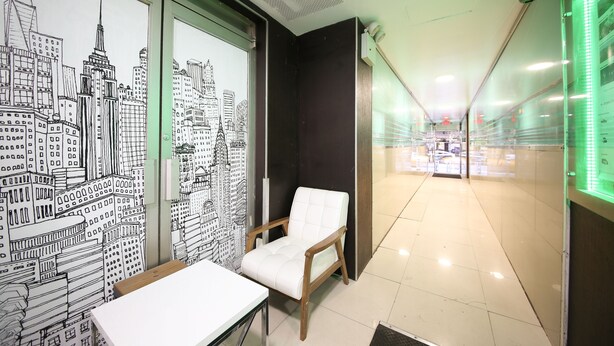 A modern interior with a cityscape mural, a white cushioned chair, and a glass partition. - Doxie Hotel (New York)