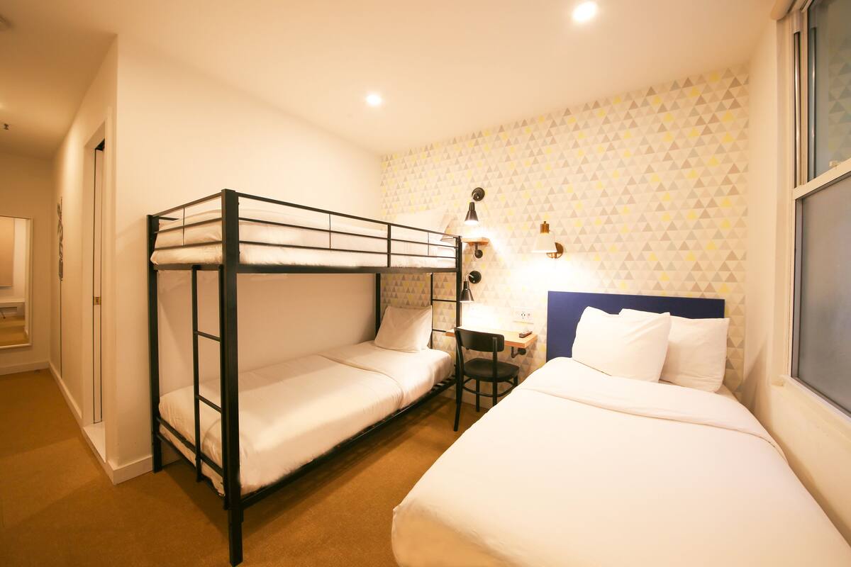 A room with bunk beds, a desk with a chair, and a wall with a geometric pattern.