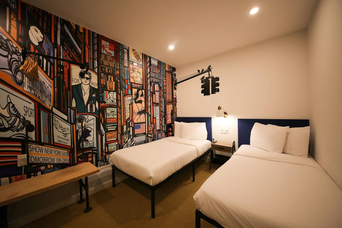 A hotel room with two single beds, a bench, and a colorful mural on the wall.