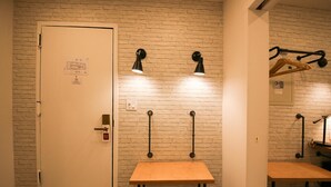 A room with a white door, a brick wall, two tables, and two wall-mounted lamps. - Doxie Hotel (New York)