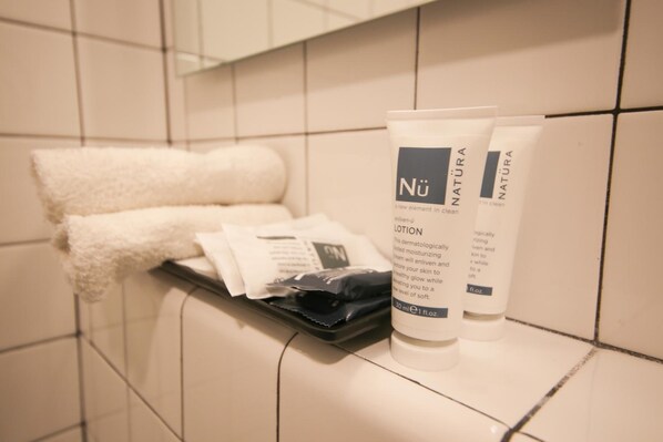 A bathroom with white tiles, a towel, and a tray with a tube of lotion and a packet.