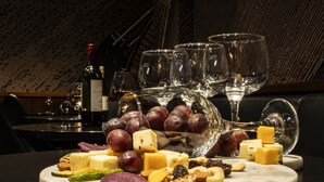 En skiferplanke med forskellige oste, druer og nødder på et marmorbord, sammen med vinglas og en flaske vin.