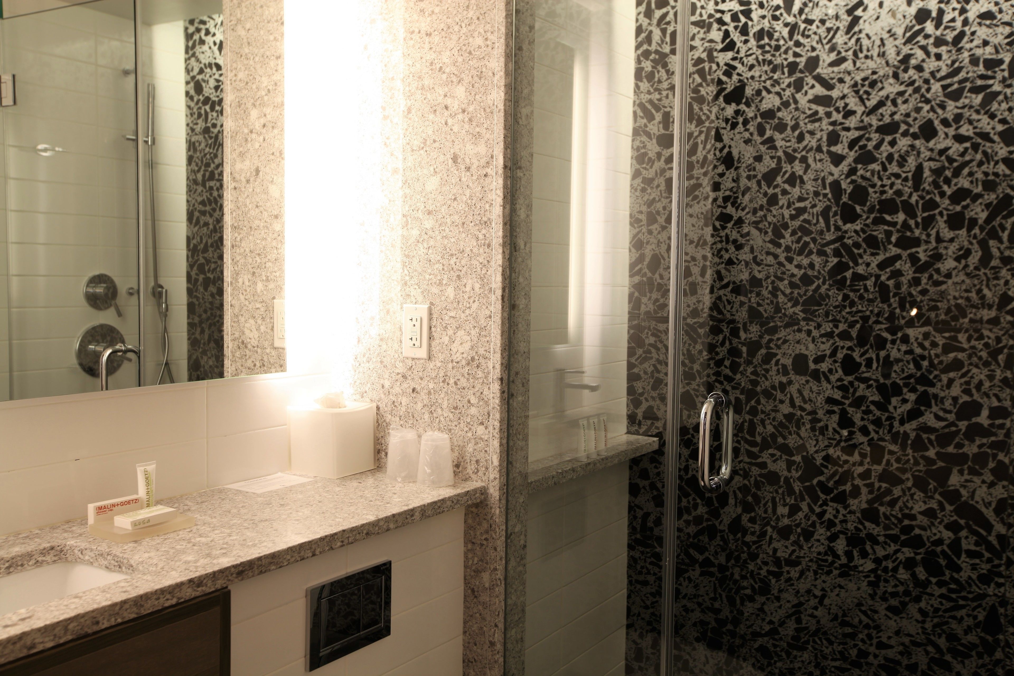 A bathroom with a granite countertop, a glass shower enclosure, and a mirror.