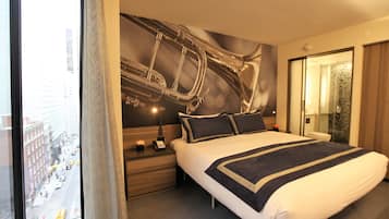 Habitación de hotel con una cama grande, una mesita de noche, un teléfono en la pared y vistas a la ciudad desde la ventana.