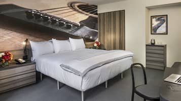 A modern hotel room with a large bed, a desk with a laptop, a chair, and a small table with a vase of flowers.
