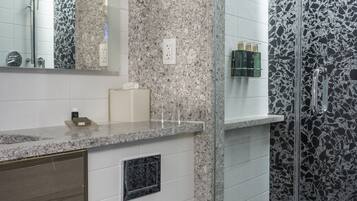 A modern bathroom with a white toilet, granite countertops, a hair dryer, and a shower with a glass door.