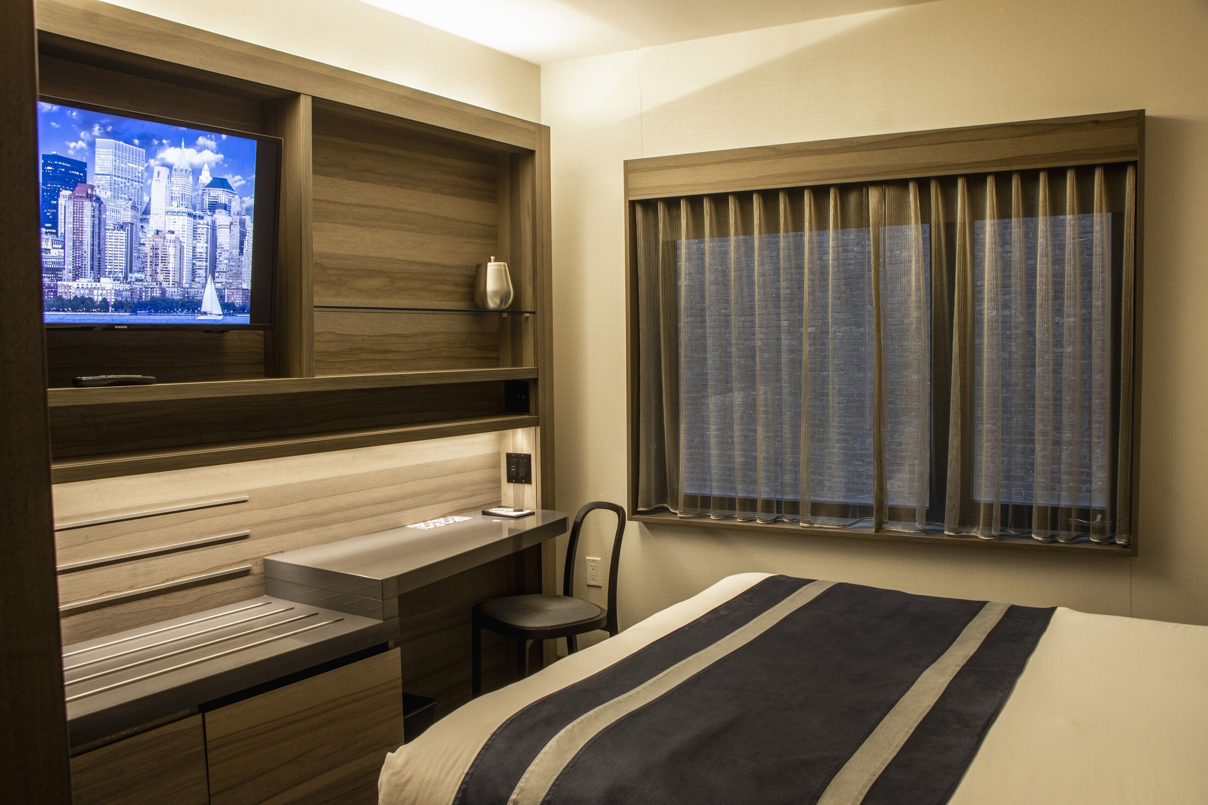 A hotel room with a bed, a desk, a chair, a television, and a window with curtains.