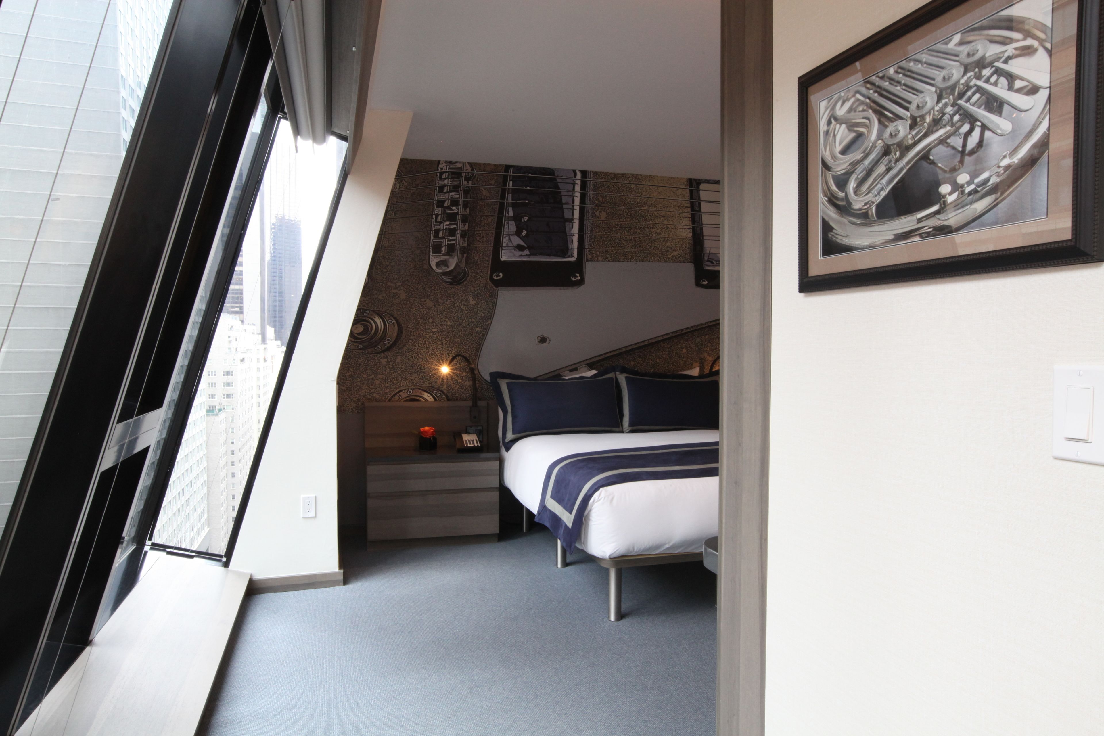 Quarto compacto com uma cama, uma secretária pequena e uma janela com vista para a cidade.
