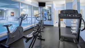 Un gimnasio con bicicletas estáticas, una cinta de correr y una piscina visibles a través de paredes de vidrio.