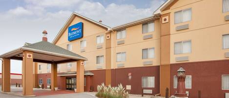 Un hotel Baymont Inn & Suites con entrada cubierta, varias ventanas y un pequeño jardín con rocas y plantas.