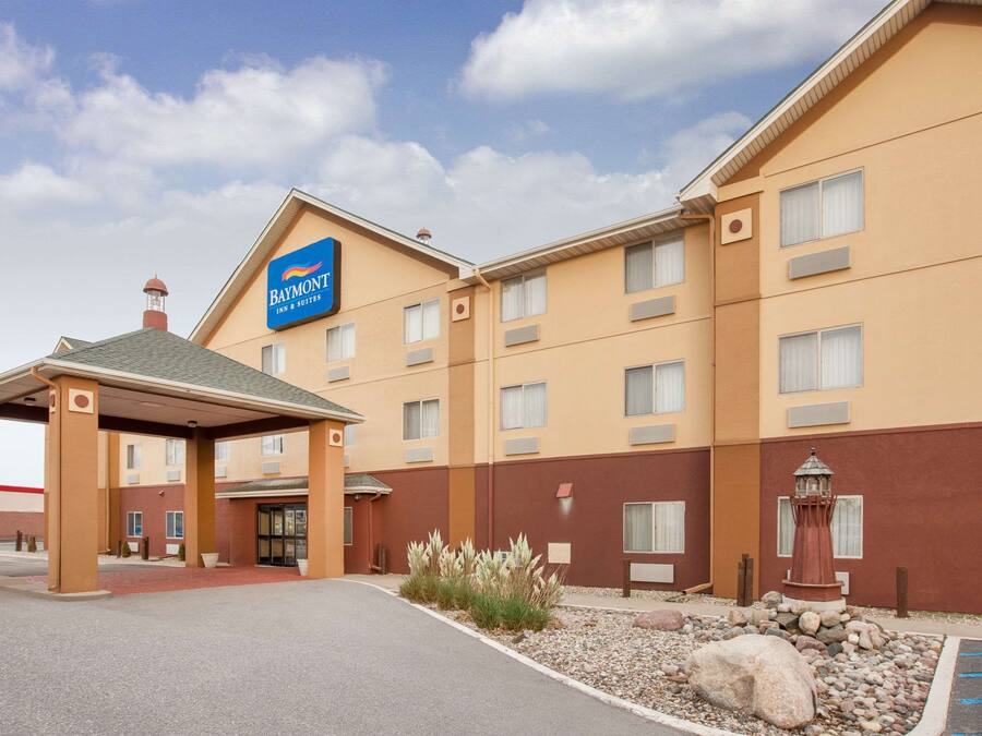 A Baymont Inn & Suites hotel with a covered entrance, multiple windows, and a small garden area with rocks and plants.
