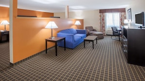 Habitación de hotel con un sofá azul, dos lámparas, un escritorio, un televisor y una alfombra estampada.