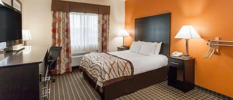 A hotel room with a bed, two bedside tables, a desk with a chair, a television, and a window with curtains.
