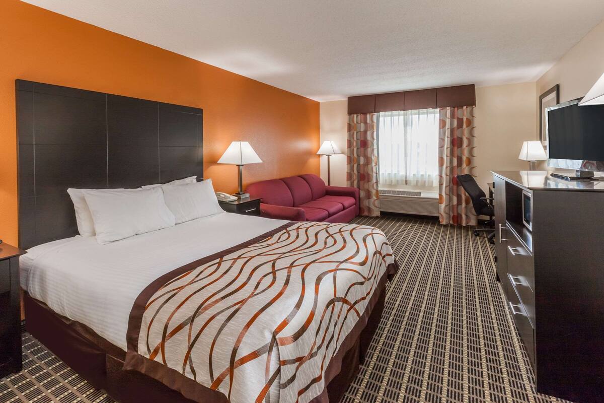 A hotel room with a large bed, a desk, a chair, a sofa, and a television.