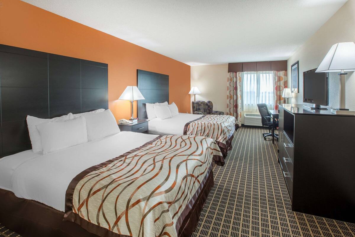 A hotel room with two beds, a desk, a chair, and a TV.