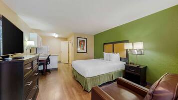 Habitación de hotel con cama, escritorio, computadora, silla, televisor y mesita de noche con lámpara.