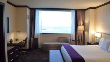 A hotel room with a bed, a desk, a chair, a small sofa, a lamp, and a view of the ocean.