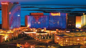 Un hotel con varias edificaciones, incluyendo un llamativo letrero de Harrah's, rodeado de un estacionamiento y vistas al océano.