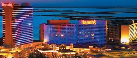 A hotel with multiple buildings, including a prominent Harrah's sign, surrounded by a parking area and a view of the ocean.