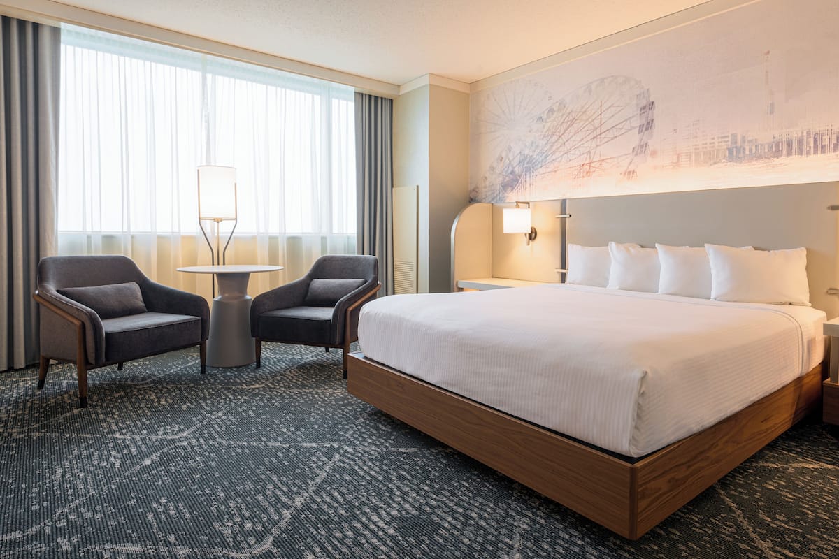 Ein Hotelzimmer mit einem großen Bett, zwei Sesseln, einem kleinen Tisch und einer Wandleuchte.