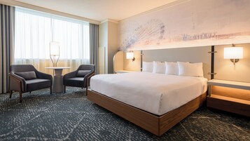 Habitación de hotel con una cama grande, dos sillones, una mesita y una lámpara fijada a la pared.