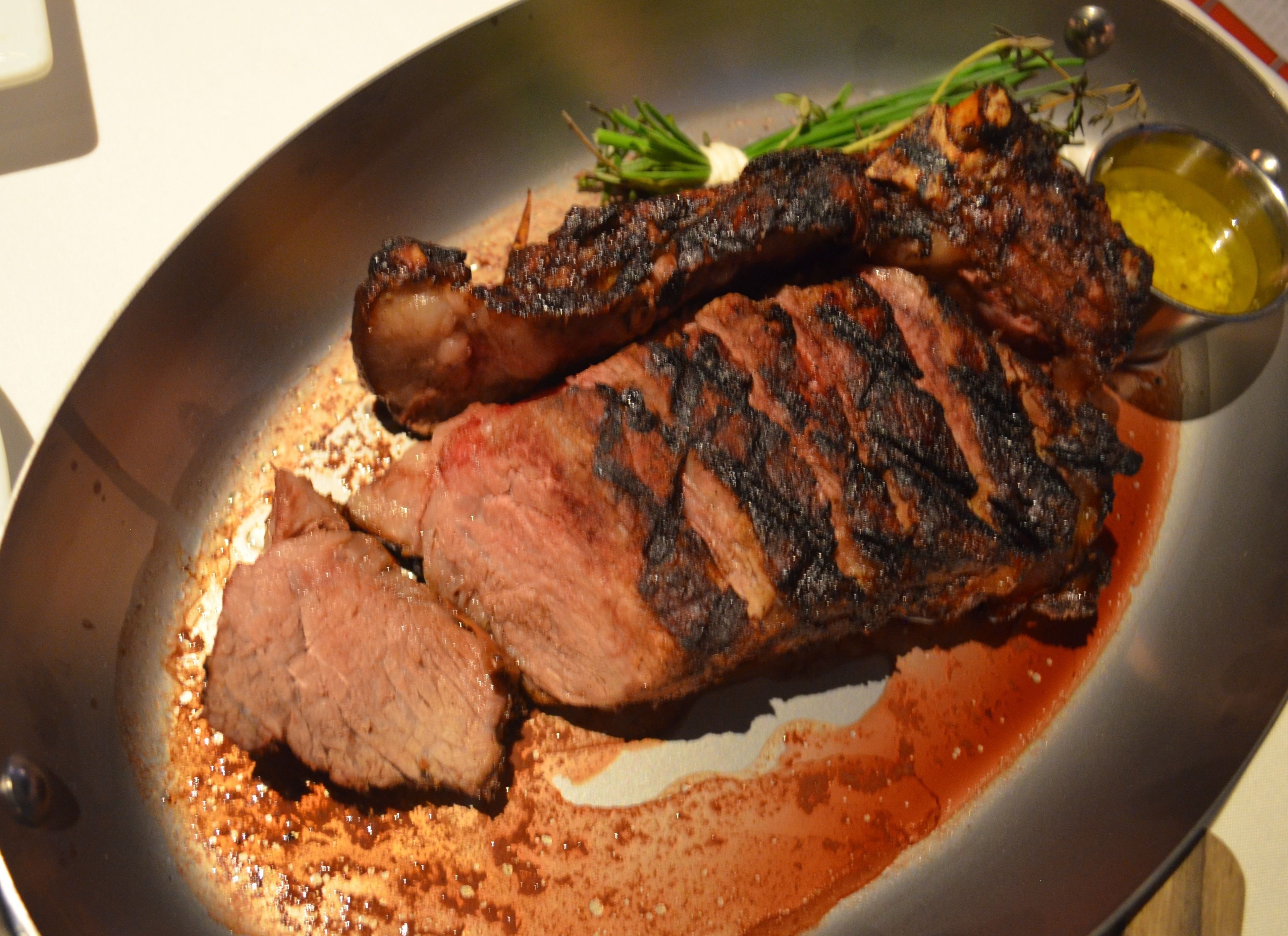Un steak à l’extérieur légèrement brûlé, servi dans une assiette avec une sauce et des herbes en accompagnement.