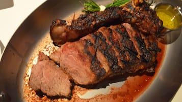 Un steak à l’extérieur légèrement brûlé, servi dans une assiette avec une sauce et des herbes en accompagnement.