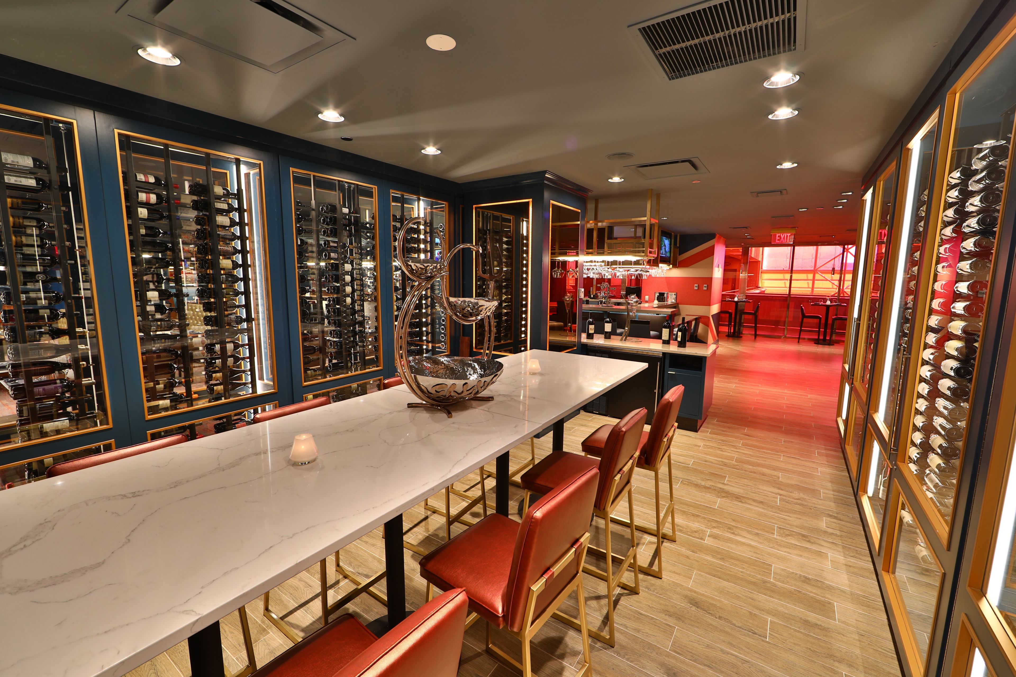 A restaurant with a long marble counter, red chairs, and wine racks.