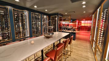 A restaurant with a long marble counter, red chairs, and wine racks.