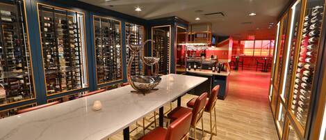 A restaurant with a long marble counter, red chairs, and wine racks.