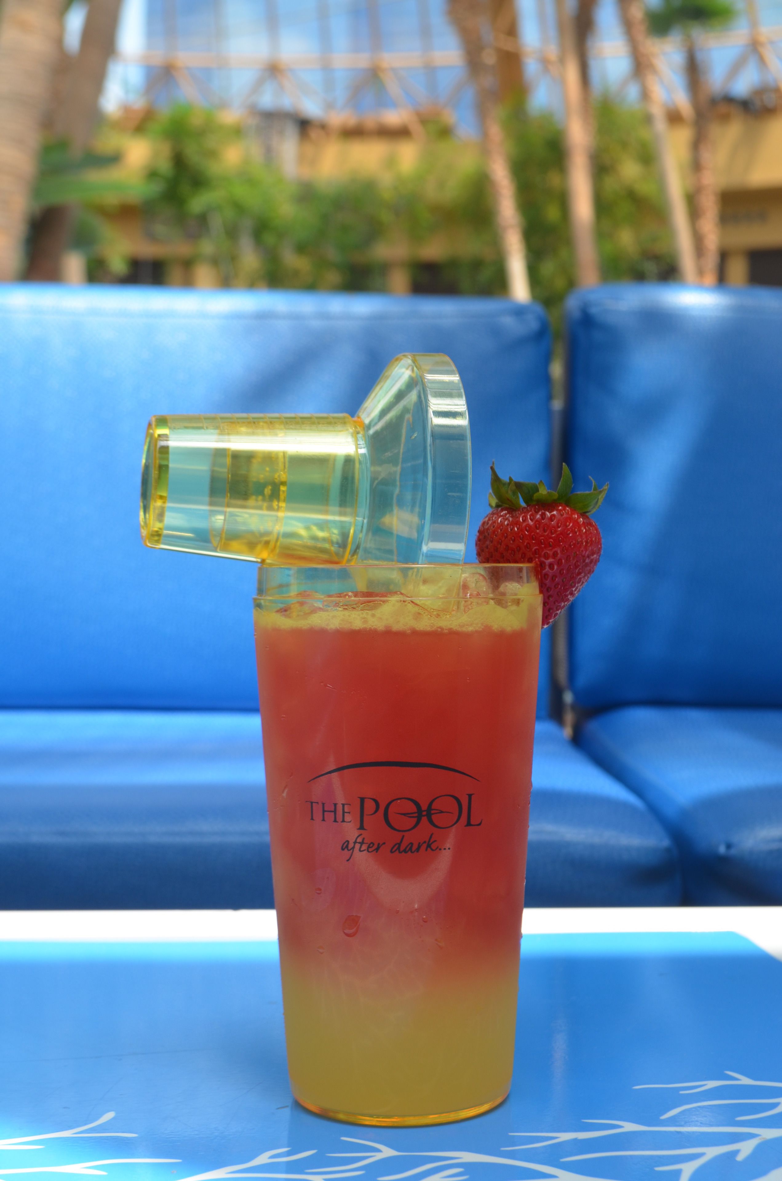 A cocktail with a strawberry garnish and a bottle cap, placed on a table with a blue couch in the background.