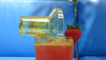 A cocktail with a strawberry garnish and a bottle cap, placed on a table with a blue couch in the background.