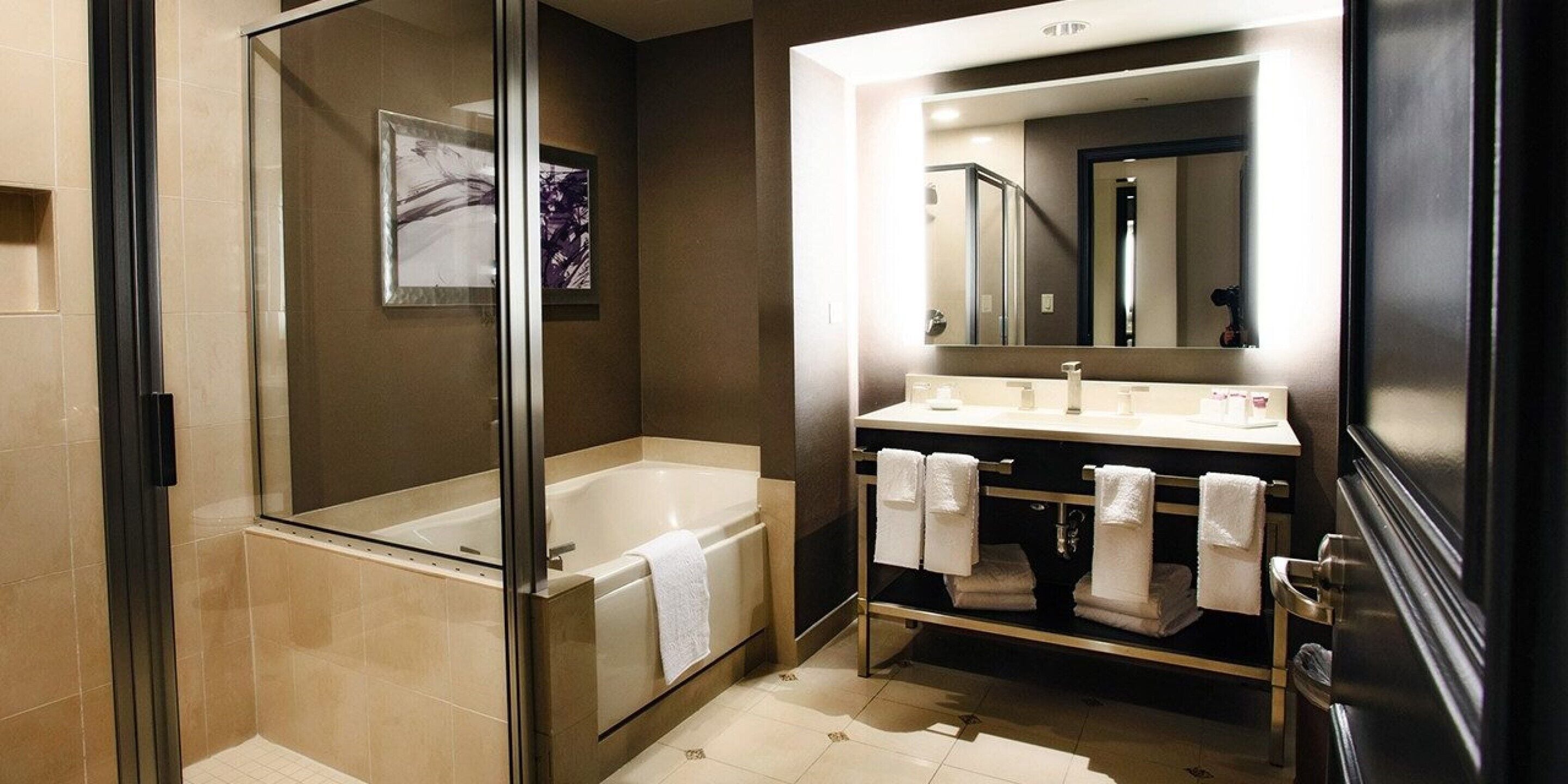 A modern bathroom with a glass-enclosed shower, a large mirror, and a vanity with multiple sinks and towels.