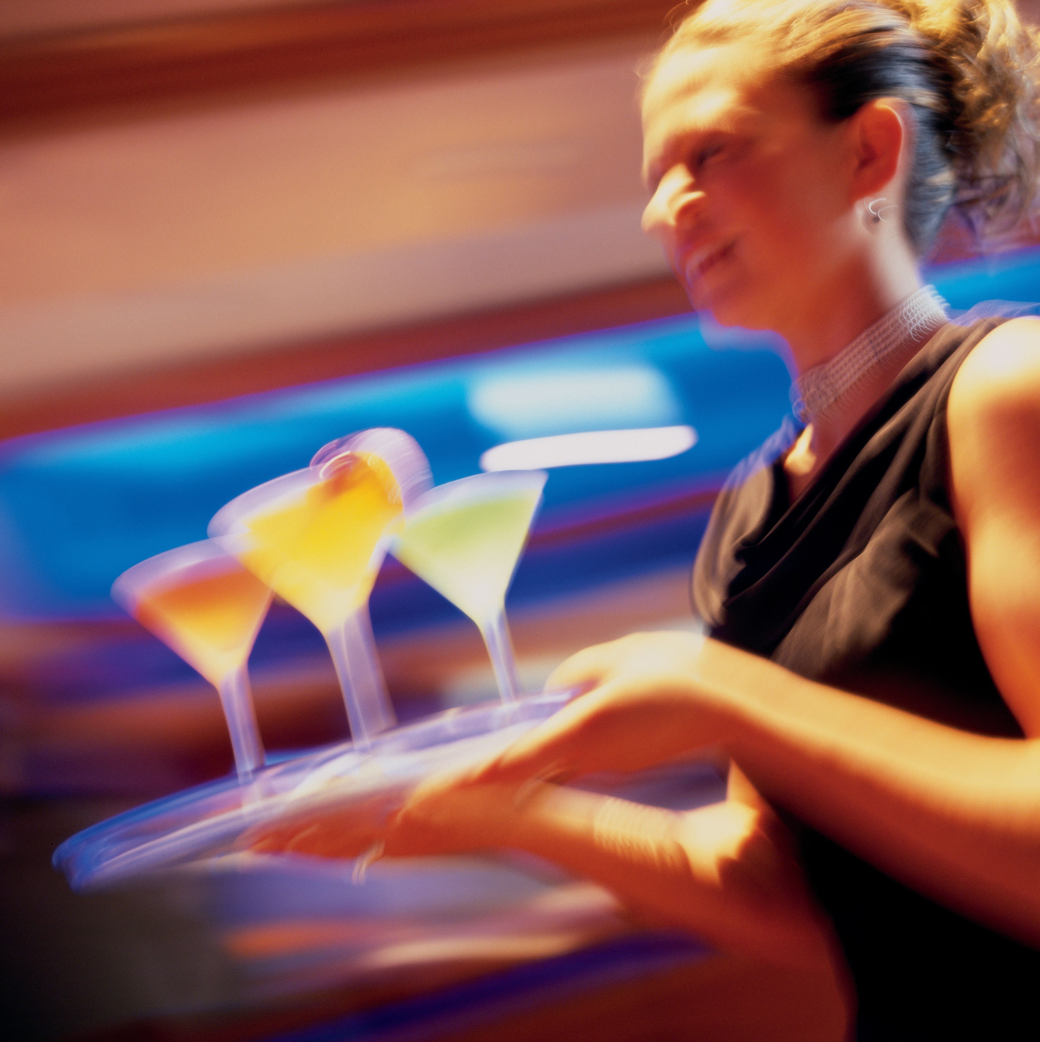 Une personne tenant un plateau sur lequel se trouvent trois verres à cocktail.