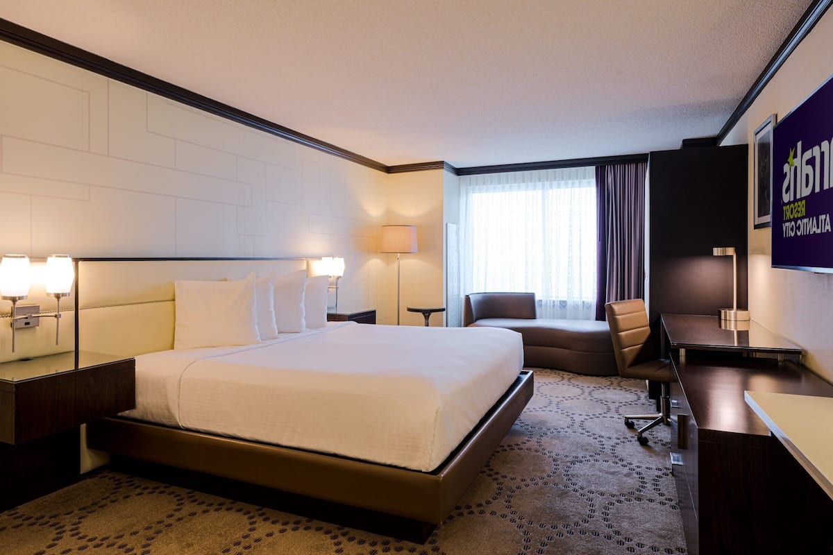 Ein Hotelzimmer mit einem großen Bett, einem Schreibtisch, einem Stuhl, einer Lampe und einem Fernseher.