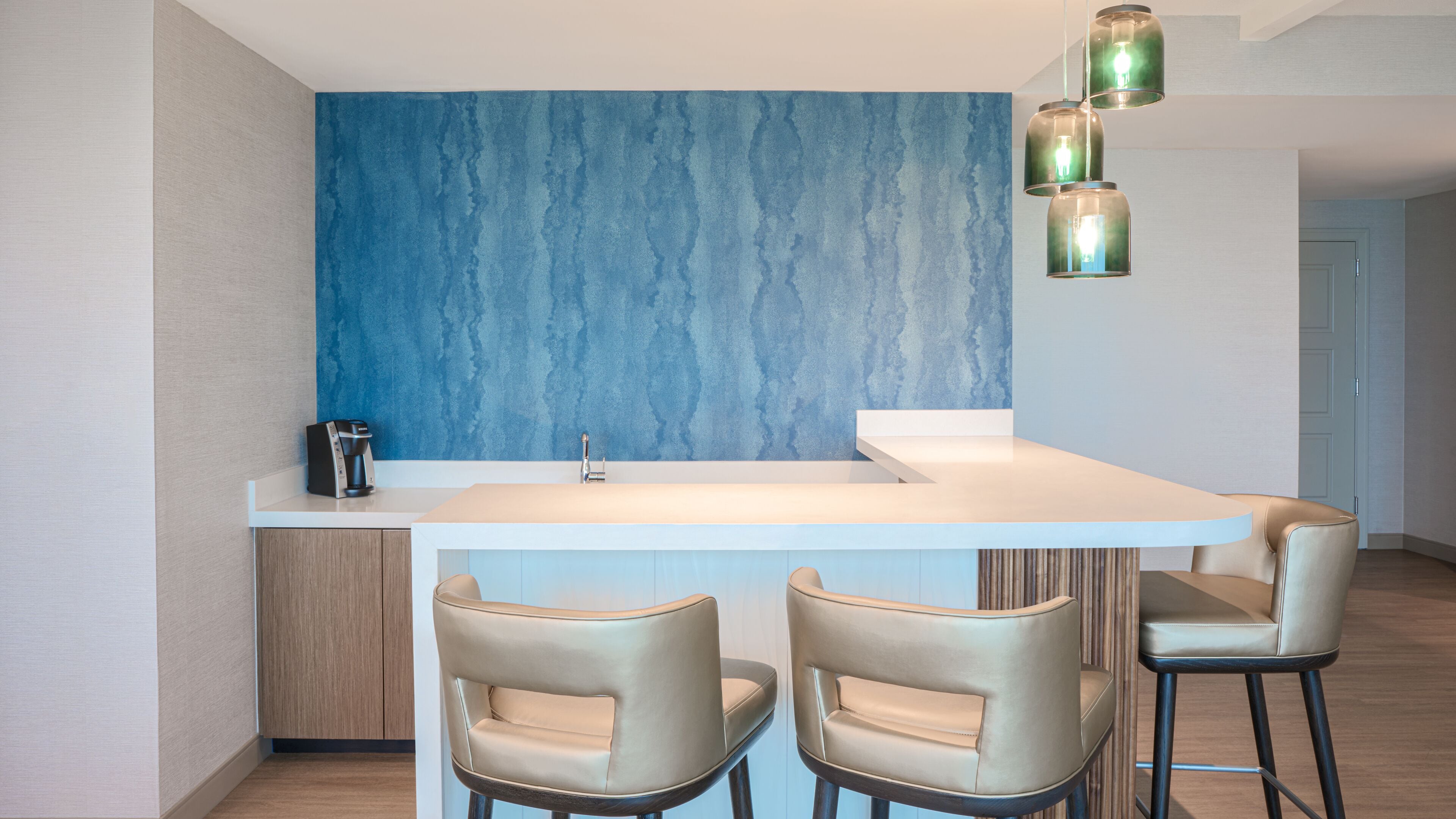 A modern kitchen with a blue accent wall, a white countertop, and two bar stools.