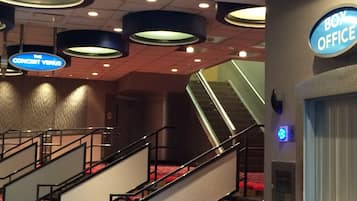 Interior de un hotel con una escalera, un letrero que dice 'Box Office' y un letrero que indica 'Concert Venue'.