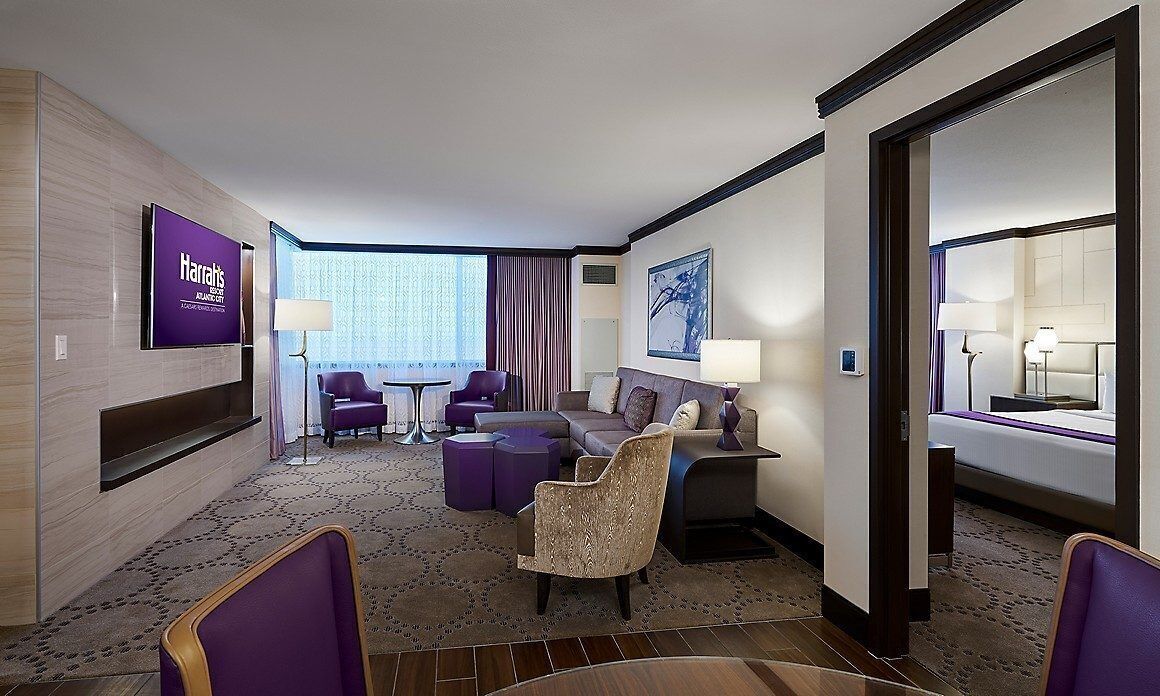 Une chambre d’hôtel équipée d’un téléviseur à écran plat, d’un canapé, d’un fauteuil, d’un bureau et d’une fenêtre avec des rideaux.