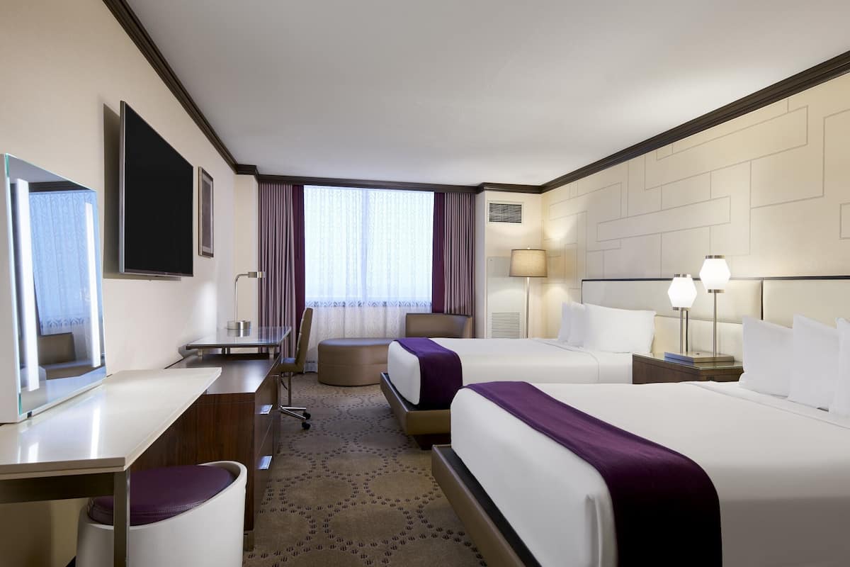 Ein Hotelzimmer mit zwei Betten, einem Schreibtisch, einem Stuhl, einer Lampe und einem großen Fenster mit Vorhängen.